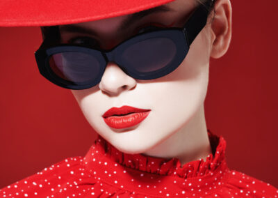 Photo de mode d'une jeune femme élégante au maquillage éclatant, vêtue d'une robe rouge, d'un chapeau rouge et de lunettes de soleil. Fond rouge. Beauté, maquillage et cosmétiques.